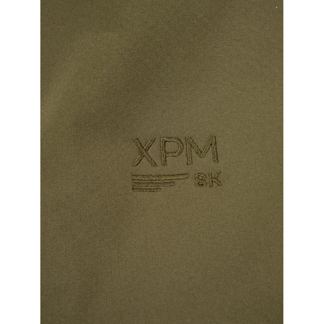 תקריב של בד בצבע ירוק זית, עליו מוטבע דגם Puffin X של Aztec עם הכיתוב "XPM 8K" רקום, שלוש קווים אופקיים מתחת, ורמז עדין לעיצוב ה-Puffin X המעניק לו מגע ייחודי.