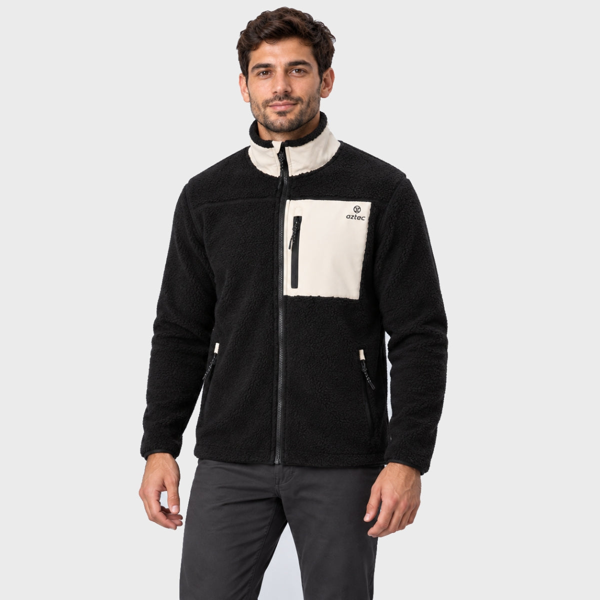 גבר לבוש במעיל פליס שחור מדגם Aztec Blizzard Sherpa Full Zip עם צווארון גבוה בצבע שמנת וכיס חזה בצבע מנוגד.