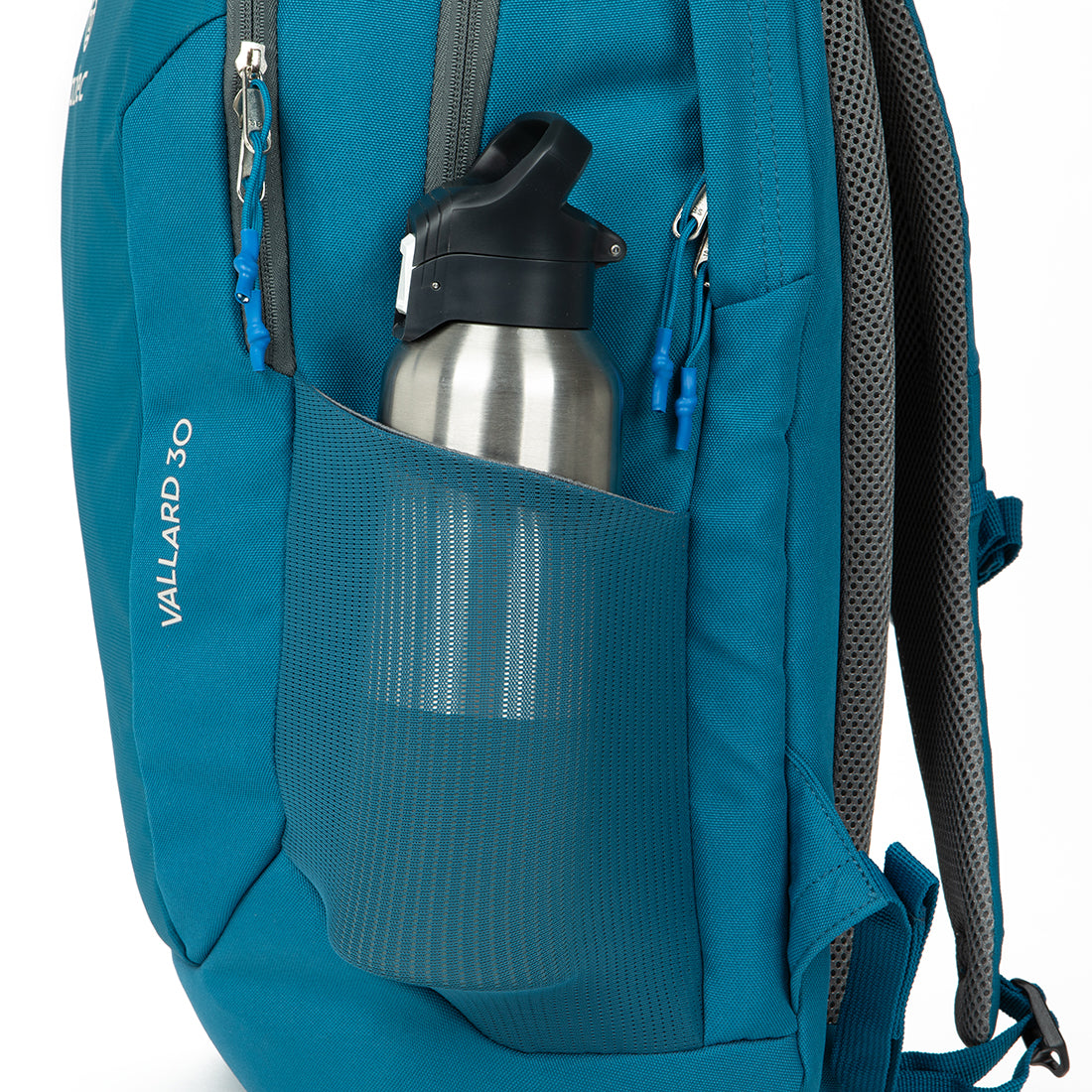 תקריב של תרמיל “Aztec Vallard 30L” כחול, עם בקבוק מים ממתכת בכיס הרשת הצדדי. לתרמיל יש רוכסנים אפורים, רצועות מרופדות ותווית עם הכיתוב “Aztec Vallard 30L” בצד.