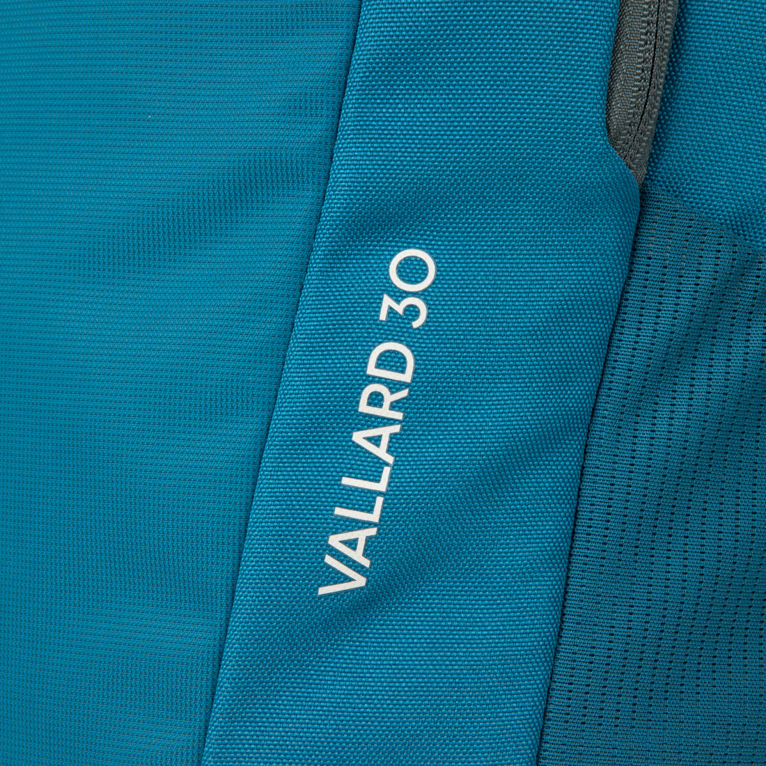 תקריב של תרמיל הבד הכחול Aztec Vallard 30L, שבו הכיתוב “VALLARD 30L” מודפס באותיות לבנות במאונך לצד הרוכסן, מה שמדגיש את העיצוב המלוטש והאלגנטי של תיק הנסיעות של Aztec.