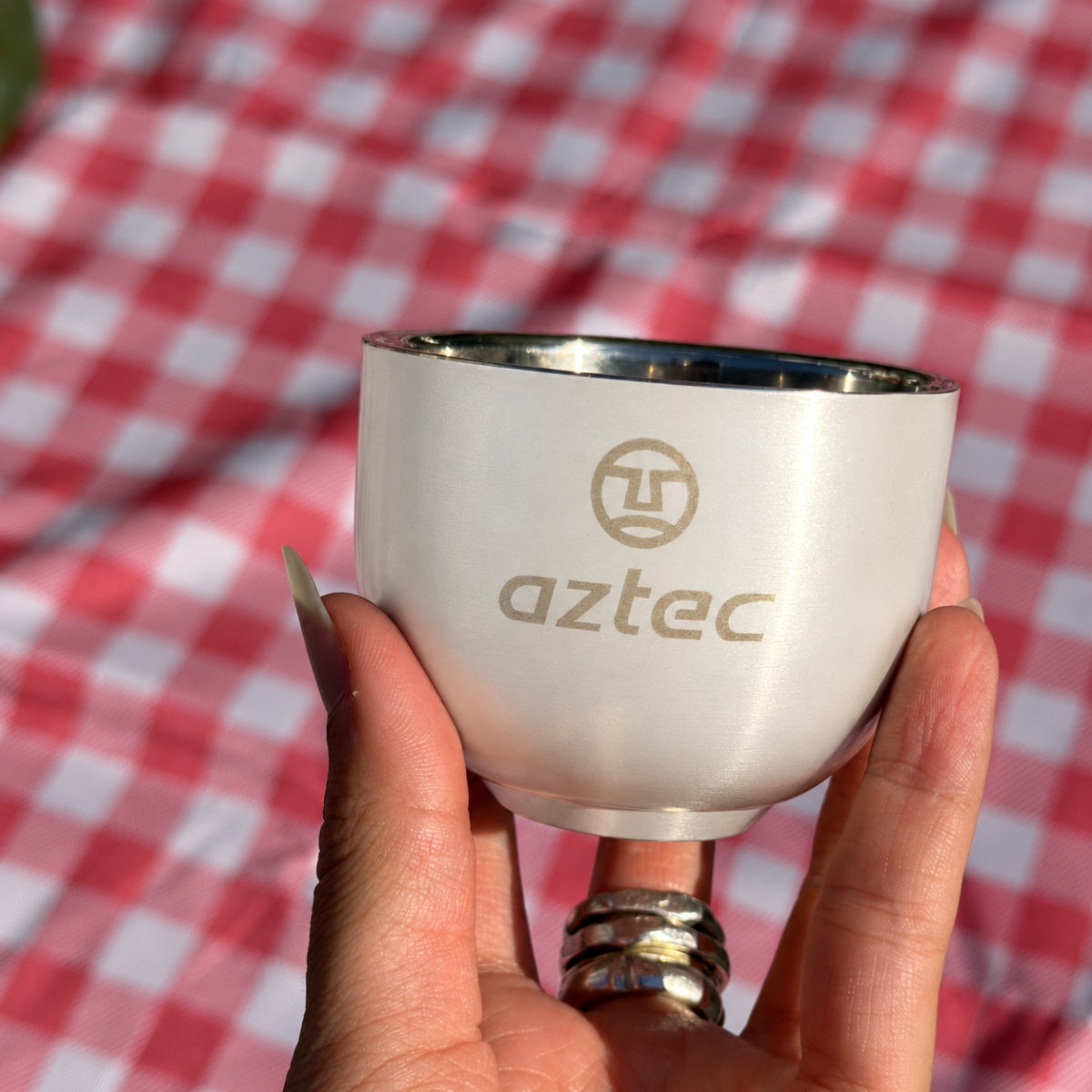 יד אוחזת באריזה של 4 כוסות קפה Aztec Coffee Cup II 120 S/S קטנות, עשויות נירוסטה כסופה, עם לוגו בצד.