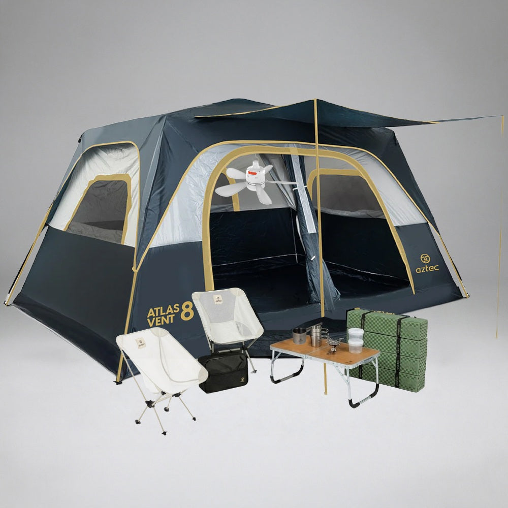 אוהל Aztec Bundle ATLAS VENT 8P בצבעי כחול ובז' הוקם בתוך הבית, כשהחלונות והדלת פתוחים. שני כסאות קמפינג לבנים, שולחן קטן עם כוסות וכד, מחצלות ירוקות וארנבון פרוותי משלימים את האווירה הנעימה.