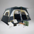 אוהל Aztec Bundle ATLAS VENT 8P בצבעי כחול ובז' הוקם בתוך הבית, כשהחלונות והדלת פתוחים. שני כסאות קמפינג לבנים, שולחן קטן עם כוסות וכד, מחצלות ירוקות וארנבון פרוותי משלימים את האווירה הנעימה.
