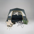 מתקן קמפינג הכולל את האוהל המרווח Aztec Bundle ATLAS VENT 6P בצבעים כחול וצהוב, בליווי שני כיסאות בצבע בז', שולחן מתקפל עם ספלים ותרמוס, קופסה ירוקה, תיק שחור ומאוורר תקרה לבן התלוי בתוך האוהל.