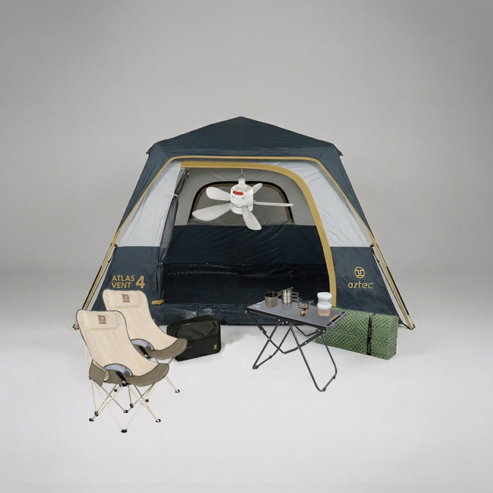 מתקן קמפינג הכולל את אוהל Aztec Bundle ATLAS VENT 4P בצבעים כחול ואפור, בליווי שני כיסאות מתקפלים בצבע בז', שולחן קטן עם ספלים וכלי מטבח, מחצלת ירוקה, תיק שחור ומאוורר תקרה בתוך האוהל — הכול מסודר על רקע אחיד.